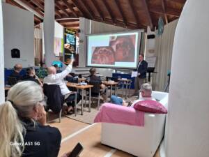 Dr n. med. Michał Czarnowski, Dyrektor Medyczny CZAR-DENT, prowadzi ekspercki wykład z zakresu zaawansowanej implantologii podczas sympozjum ICX Study Club na Majorce. Na rzutniku w tle prezentowane są zdjęcia z klinicznego zabiegu stomatologicznego, a na sali znajduje się grupa słuchających lekarzy.